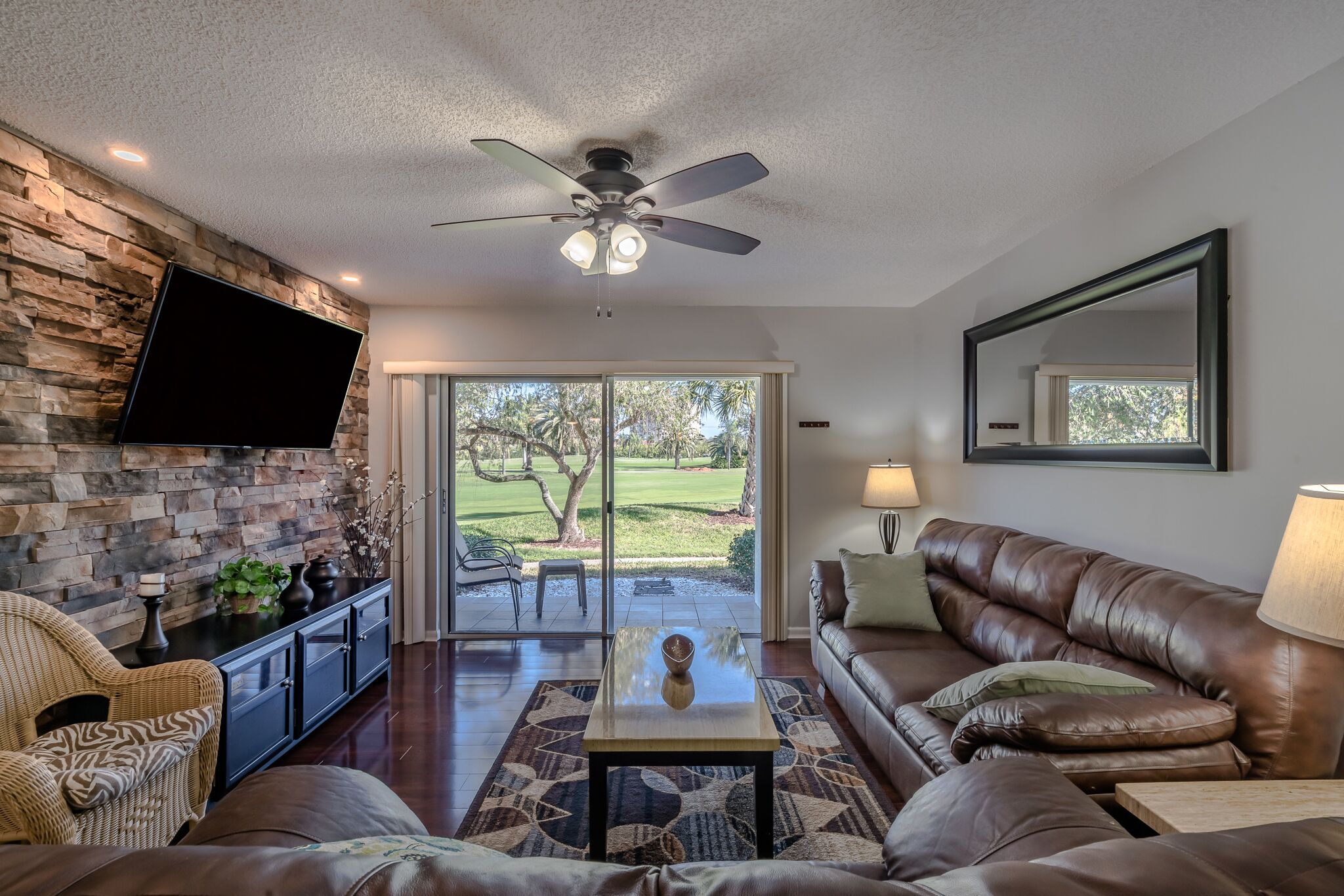Cozy living room of Isla Bliss Unit 137, a vacation rental in St. Petersburg, featuring leather seating, a mounted TV, and golf course views from the patio.