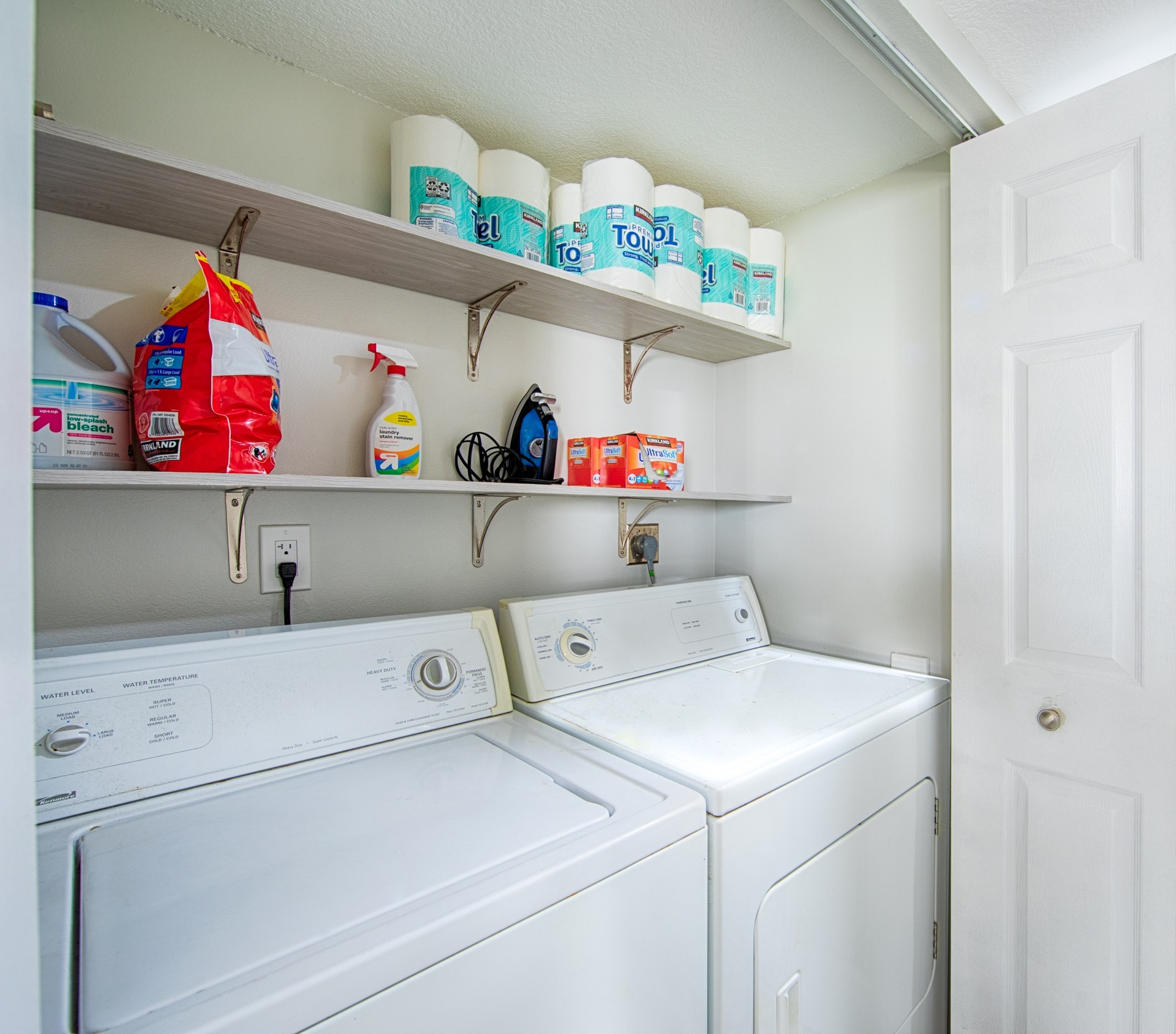 Laundry room with washer, dryer, and shelves stocked with cleaning supplies, detergent, and paper towels.