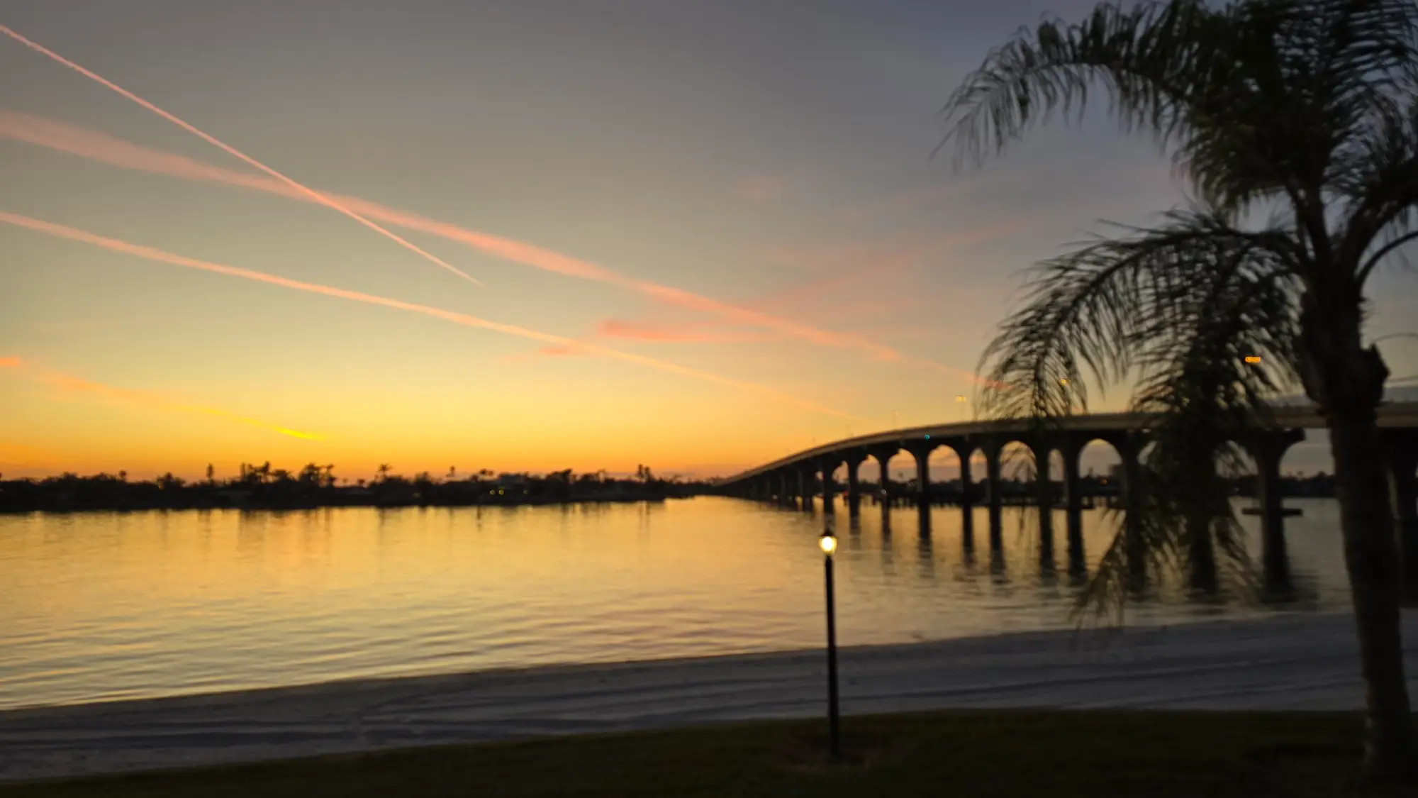 Scenic sunset view of a bridge over calm water with palm trees