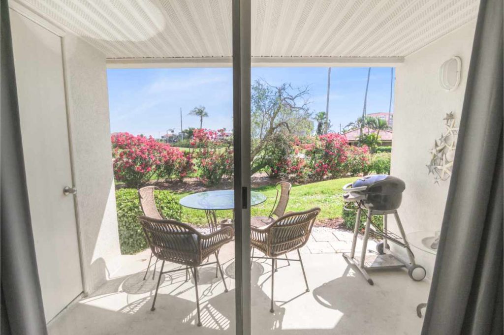 A private, ground-floor patio at an Isla Del Sol vacation rental featuring a patio table, chairs, and an electric grill overlooking tropical greenery.