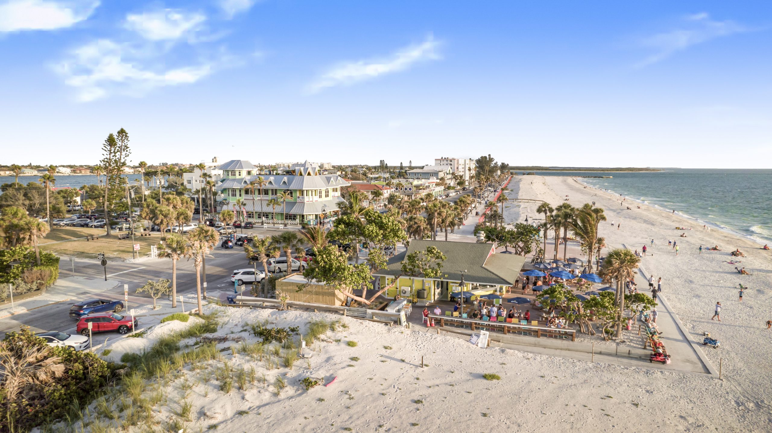 Aerial view of a beachfront restaurant and surrounding businesses along St. Pete Beach with palm trees, shoreline, and Gulf waters